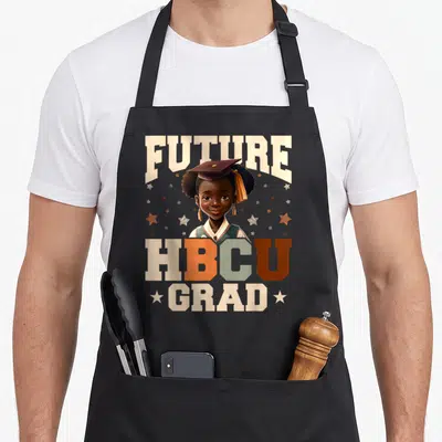 Youth future history apron - Cartoon girl in cap with FUTURE HBCU GRAD text and stars — shown on a black cotton canvas apron against a white background
