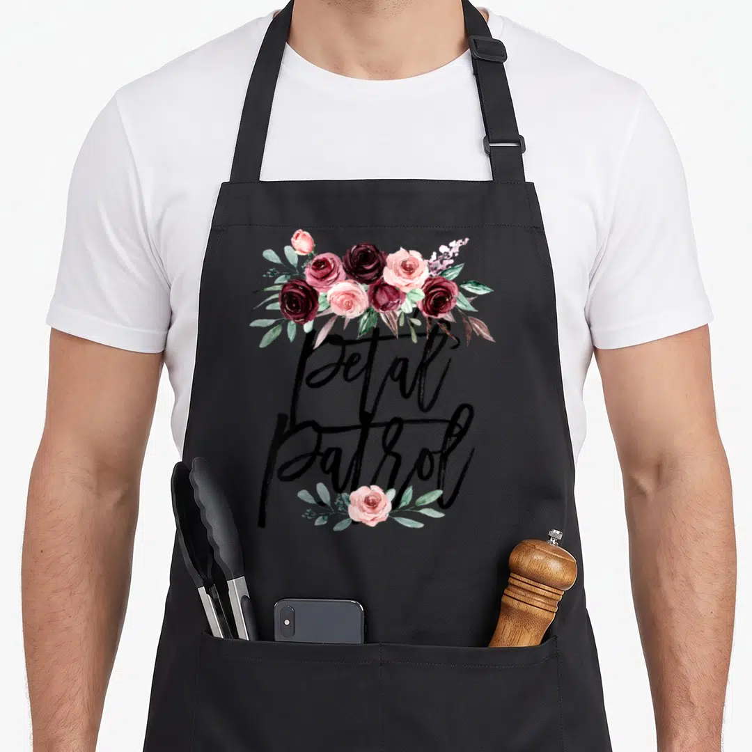 Proposal bridesmaid aprons - Petal Patrol script with red pink and green watercolor roses and leaves — shown on a black cotton canvas apron against a white background