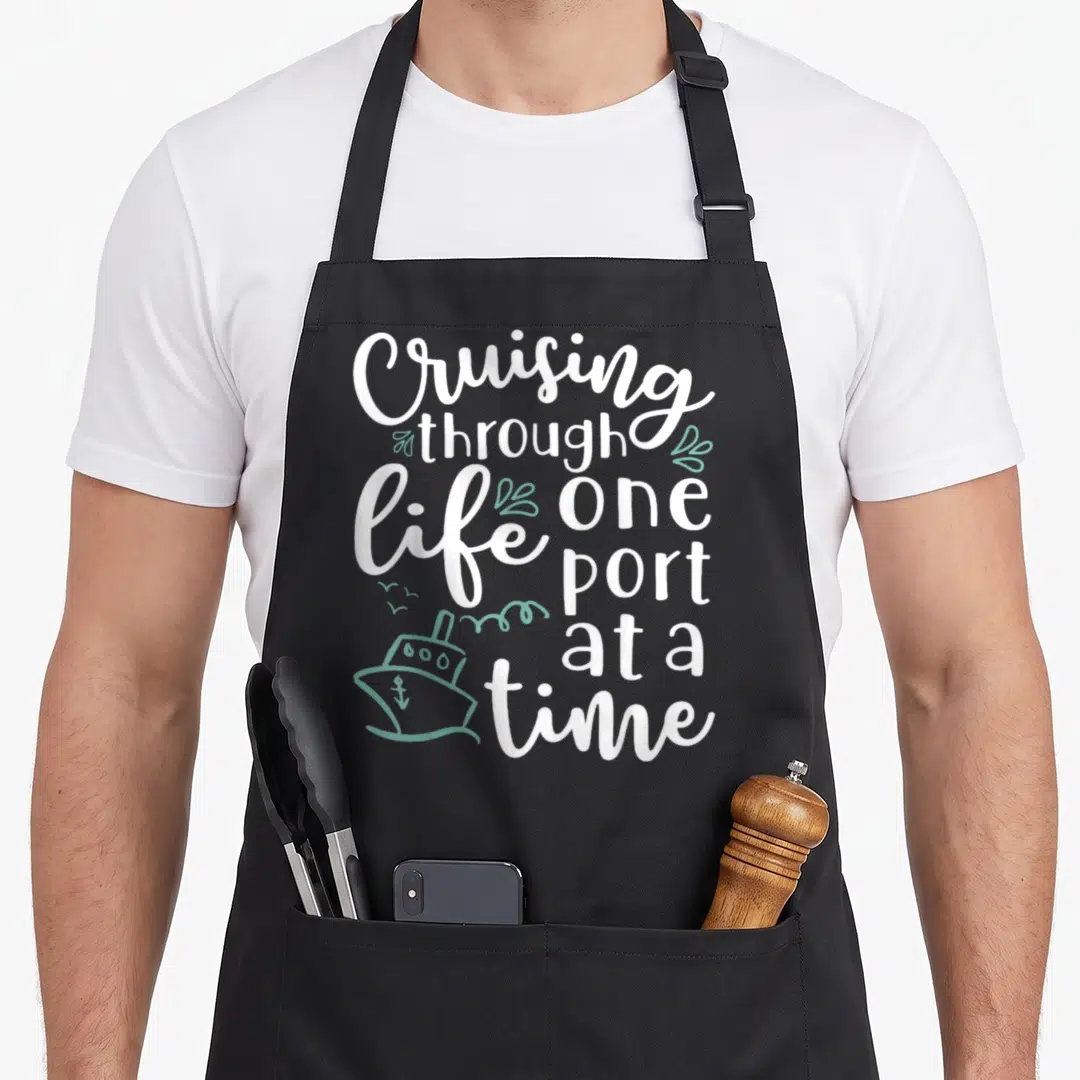 Cruising wine life apron - Stacked white text reading Cruising Through Life One Port At A Time with a mint green ship — shown on a black cotton canvas apron against a white background