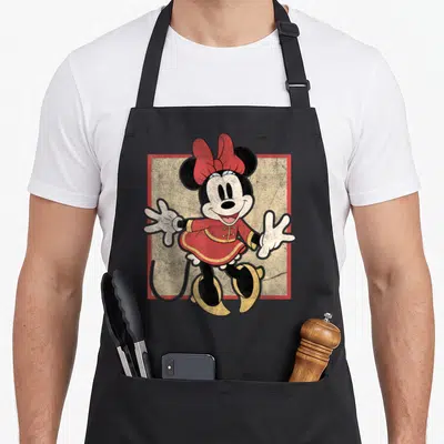 Lunar friends apron - Minnie Mouse in red dress and yellow shoes centered on textured beige background with red border — shown on a black cotton canvas apron against a white background