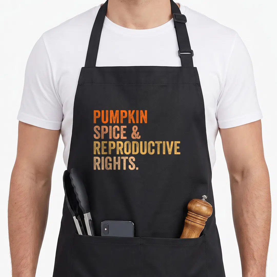 Right spice apron - Stacked PUMPKIN SPICE & REPRODUCTIVE RIGHTS text in orange peach and yellow gradients — shown on a black cotton canvas apron against a white background