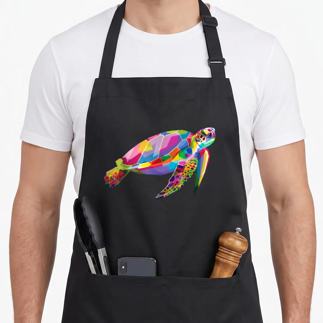 Sea colorful aprons - Multicolored cartoon sea turtle in blue, green, yellow, red, and purple geometric shapes — shown on a black cotton canvas apron against a white background