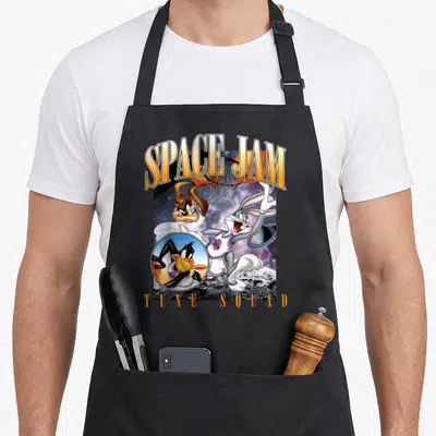 Space squad apron - Bugs Bunny jumping to hoop with Space Jam Tune Squad text and Daffy Duck circular inset — shown on a black cotton canvas apron against a white background