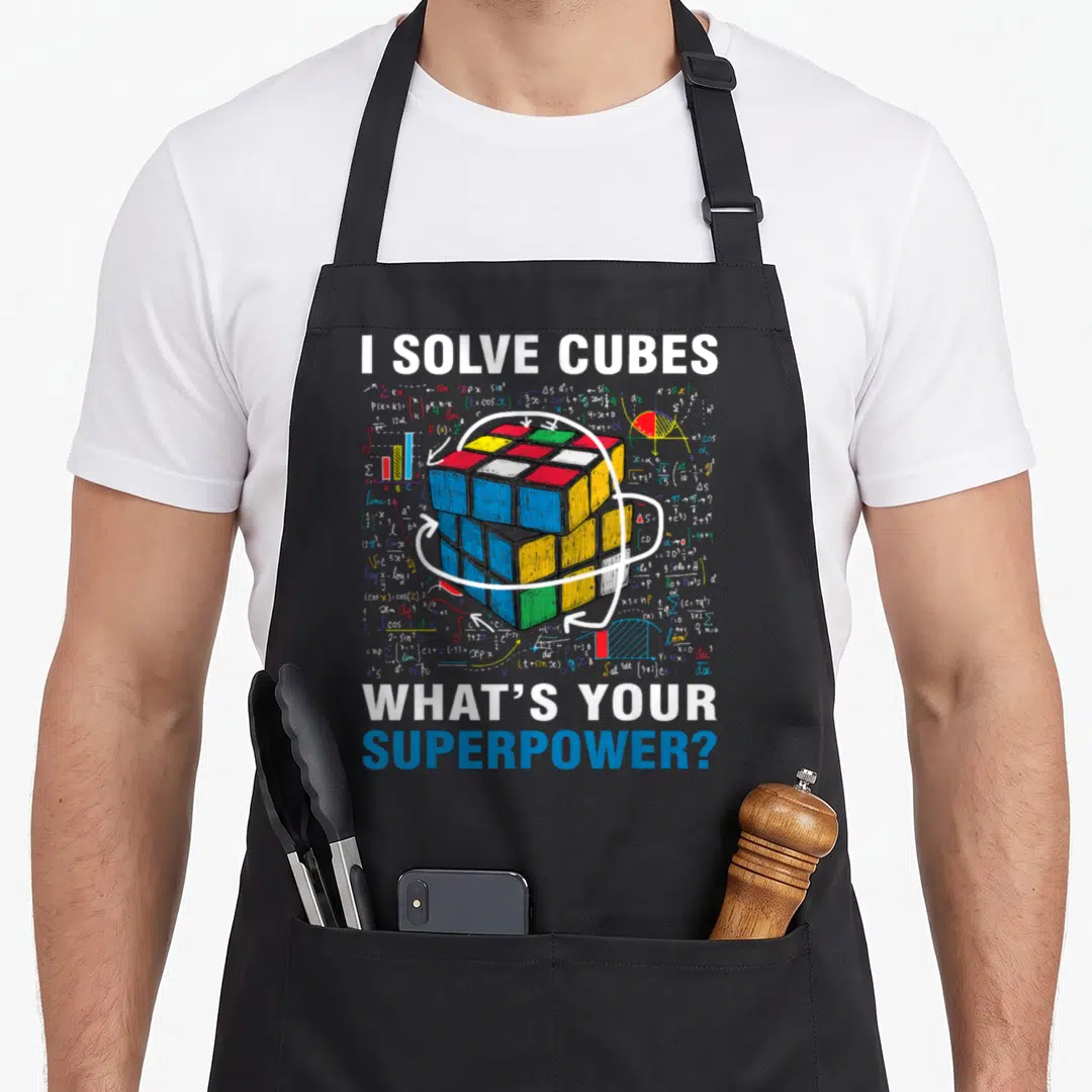 Solve rubiks cube apron - Cartoon Rubik's cube with math formulas, three rotation arrows, and text I SOLVE CUBES WHAT'S — shown on a black cotton canvas apron against a white background
