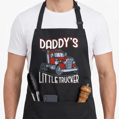 Daddy truck apron - Red cartoon semi-truck with arched DADDY'S LITTLE TRUCKER text in white and grey — shown on a black cotton canvas apron against a white background