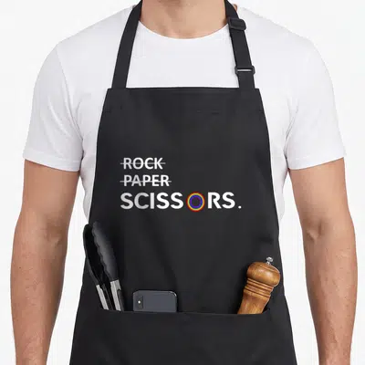 Lgbt paper apron - Rock Paper Scissors text with rainbow O and crossed out words — shown on a black cotton canvas apron against a white background