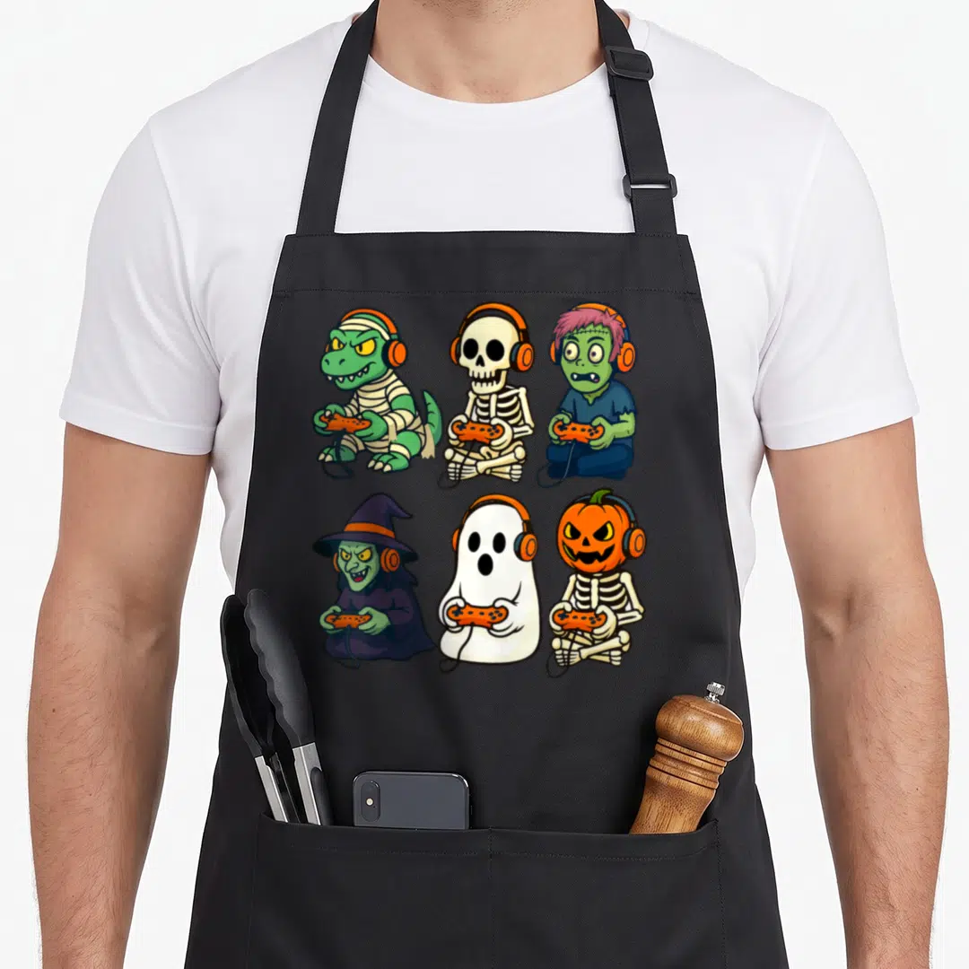 Gamer halloween witch apron - Six cartoon monsters with headphones and controllers in orange green purple white — shown on a black cotton canvas apron against a white background
