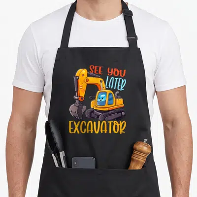 Excavator bulldozer apron - Cartoon yellow excavator with see you later text and two front pockets — shown on a black cotton canvas apron against a white background