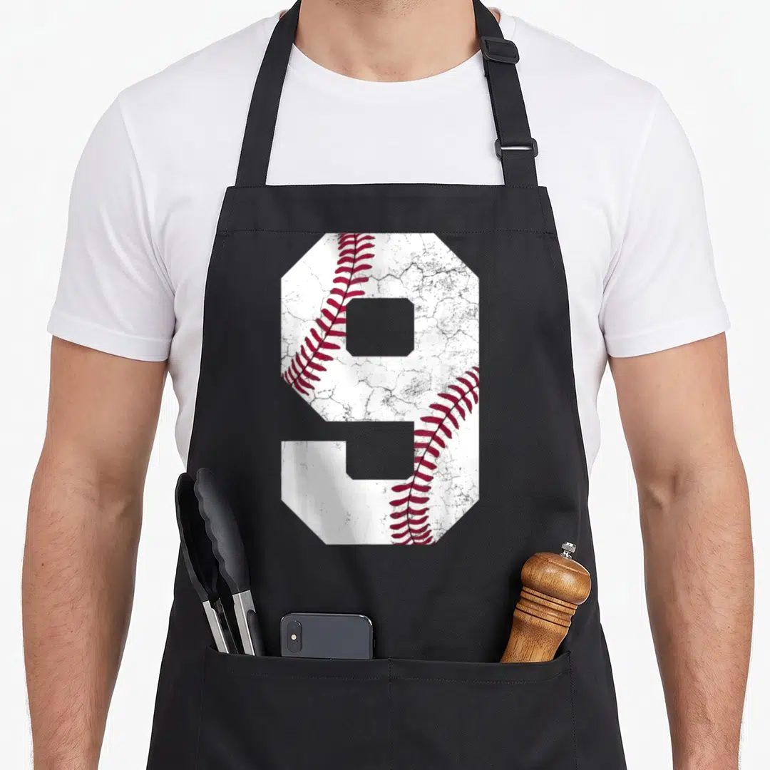 9th baseball apron - Large number nine with white cracked texture and red baseball stitching on black fabric — shown on a black cotton canvas apron against a white background