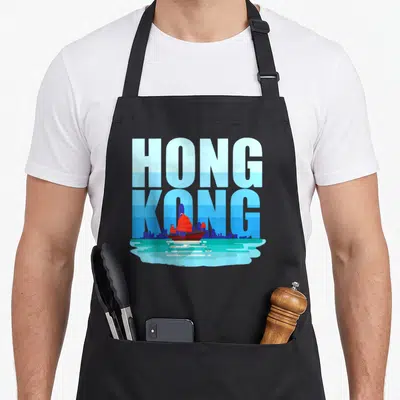 China hong kong apron - Stacked HONG KONG text behind blue skyline and red junk boat over teal water — shown on a black cotton canvas apron against a white background