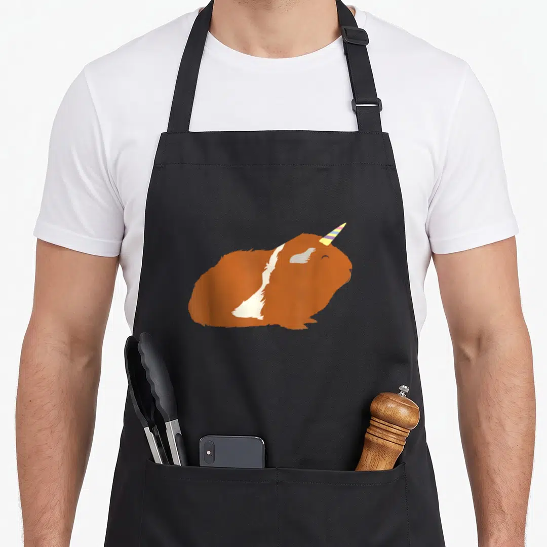 Guinicorn apron or apron - Cartoon guinea pig with rainbow striped horn resting on black fabric — shown on a black cotton canvas apron against a white background