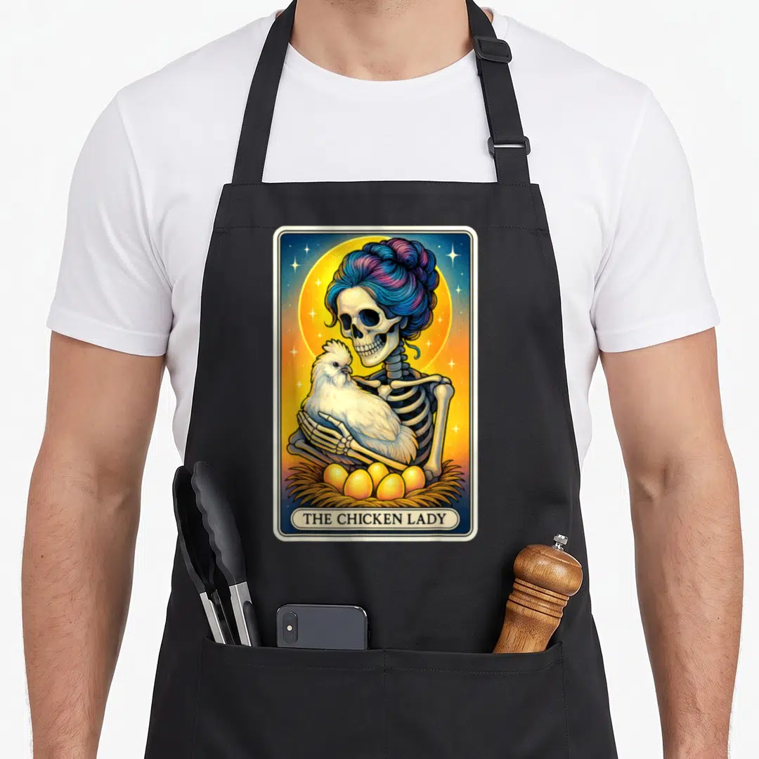 Tarot chicken with apron - Skeleton holding white chicken with nest of eggs and text The Chicken Lady — shown on a black cotton canvas apron against a white background