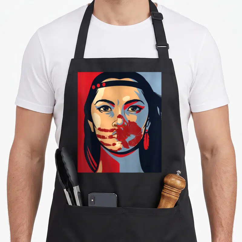 Mmiw indigenous apron - Stylized Native American woman portrait with red handprints over mouth and feather earring — shown on a black cotton canvas apron against a white background