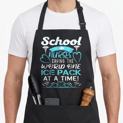 Saving nurse apron - White and blue typography reading School Nurses Saving The World One Ice Pack At A Time — shown on a black cotton canvas apron against a white background