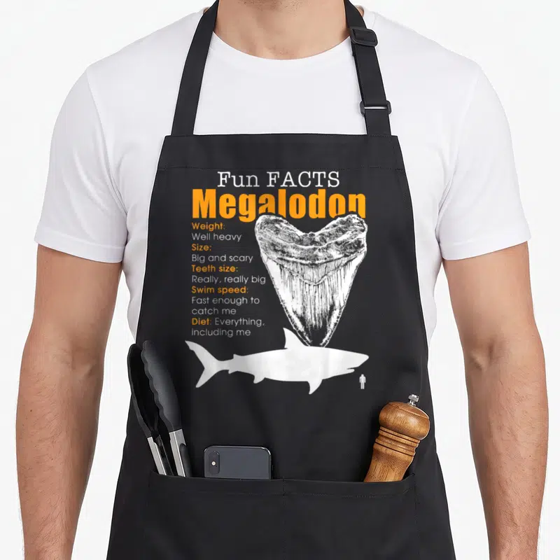 Enthusiast megalodon apron - Megalodon fun facts text, large tooth, and shark silhouette with tiny person — shown on a black cotton canvas apron against a white background