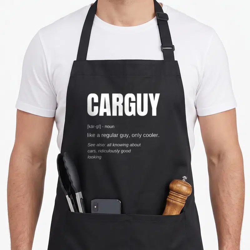 Definition car apron - White CARGUY dictionary definition text stacked on black fabric background — shown on a black cotton canvas apron against a white background