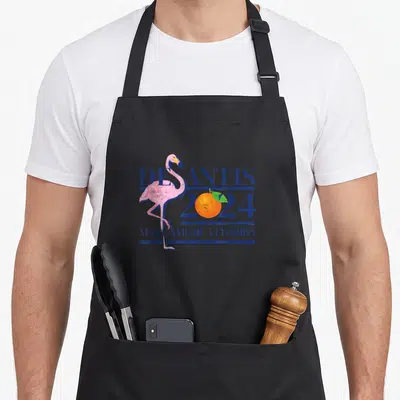 Desantis florida apron - Pink flamingo overlaps blue DESANTIS 2024 text with orange in zero and Make America Florida — shown on a black cotton canvas apron against a white background
