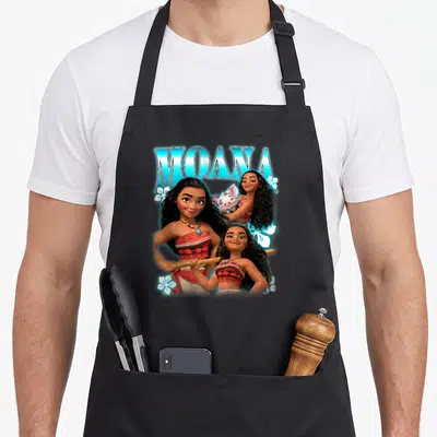 Brave novelty apron - Three Moana figures and Pua pig with blue MOANA text and white flowers — shown on a black cotton canvas apron against a white background