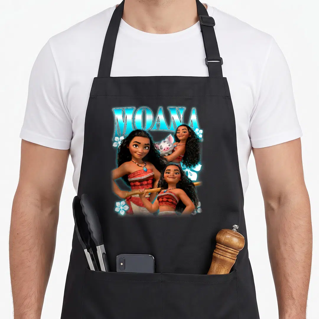 Brave novelty apron - Three Moana figures and Pua pig with blue MOANA text and white flowers — shown on a black cotton canvas apron against a white background