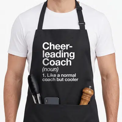 Coach cheerleading apron - White dictionary definition text reading Cheerleading Coach on a grey background — shown on a black cotton canvas apron against a white background