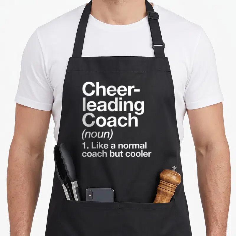 Coach cheerleading apron - White dictionary definition text reading Cheerleading Coach on a grey background — shown on a black cotton canvas apron against a white background