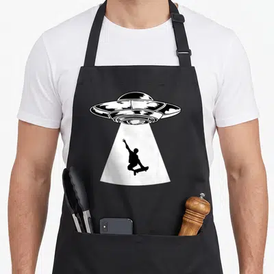 Skater skateboarding skateboard funny apron - Black and white UFO line art abducting a skateboarder silhouette — shown on a black cotton canvas apron against a white background