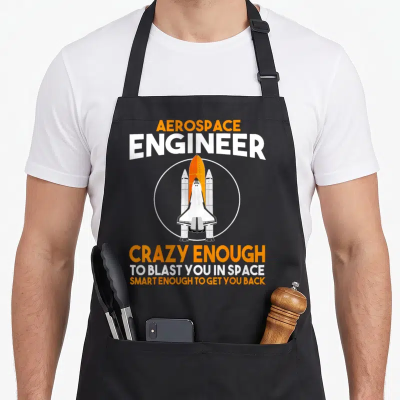 Blast engineer apron - Space shuttle in white circle with orange and black text reading Aerospace Engineer Crazy Enough — shown on a black cotton canvas apron against a white background