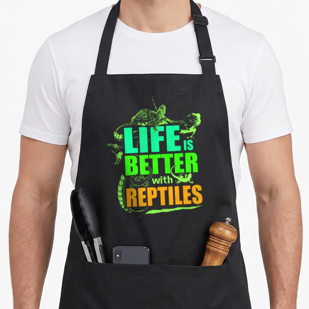 Better reptile leopard apron - Stacked LIFE BETTER REPTILES text in turquoise lime and orange with cartoon reptiles — shown on a black cotton canvas apron against a white background