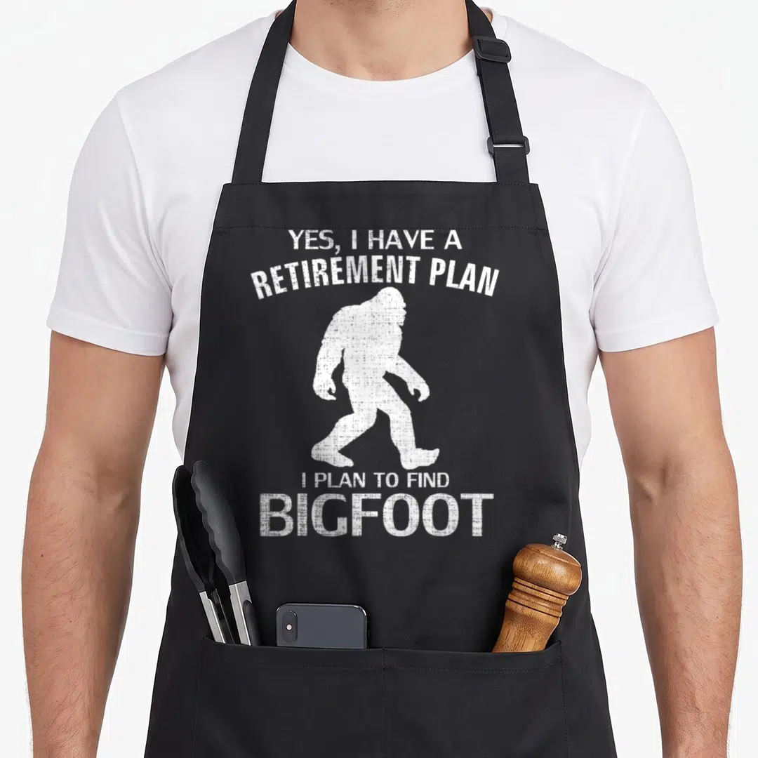 Plan retirement apron - White distressed Bigfoot silhouette with Yes I Have a Retirement Plan I Plan to Find Bigfoot — shown on a black cotton canvas apron against a white background
