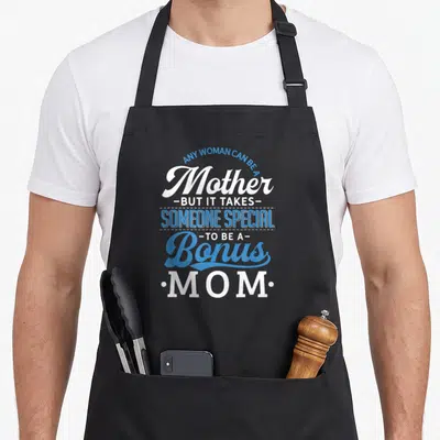 Stepmother mother's day aprons - Blue and white typography reading Any Woman Can Be A Bonus Mom stacked vertically — shown on a black cotton canvas apron against a white background