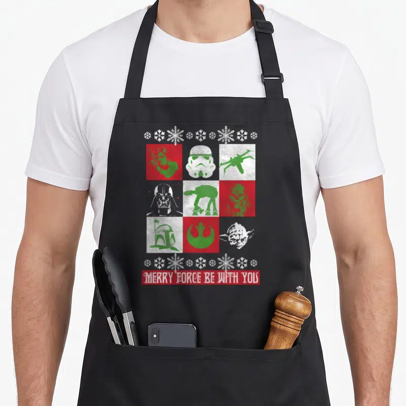 Funny force merry christmas apron - Star Wars silhouettes in red green white grid with Merry Force Be With You text — shown on a black cotton canvas apron against a white background