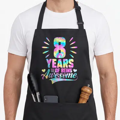 8th tie apron - Tie-dye number 8 with Years of Being Awesome text and two hearts — shown on a black cotton canvas apron against a white background
