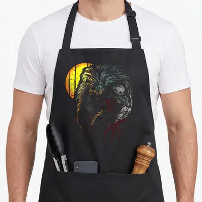 Lycan halloween apron - Realistic grey werewolf with red claws in front of a yellow sun and tree silhouettes — shown on a black cotton canvas apron against a white background