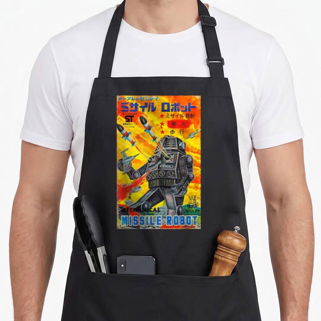 Missile anime apron - Retro robot illustration with flying missiles, Japanese text, and yellow orange background — shown on a black cotton canvas apron against a white background