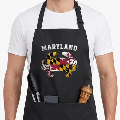 Blue crab apron - Arched MARYLAND text above a crab filled with red yellow black and white flag patterns — shown on a black cotton canvas apron against a white background