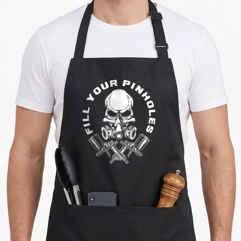 Fill painter apron - White skull in respirator with two crossed spray guns and arched text — shown on a black cotton canvas apron against a white background