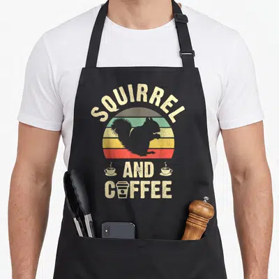 Squirrel pet apron - Retro squirrel silhouette in striped sun with text squirrel and coffee and three mugs — shown on a black cotton canvas apron against a white background