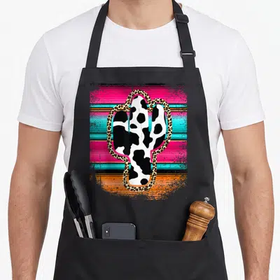 Western cactus apron - Cow print cactus with leopard border on pink, turquoise, and orange horizontal stripes — shown on a black cotton canvas apron against a white background