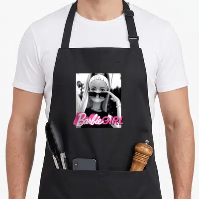 Casual general apron - Barbie GIRL pink text over black and white doll photo with sunglasses — shown on a black cotton canvas apron against a white background