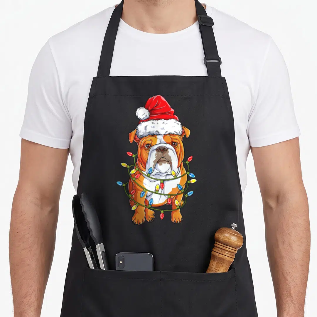 Santa english chef aprons - Cartoon bulldog in red Santa hat wrapped in red yellow blue and white Christmas lights — shown on a black cotton canvas apron against a white background