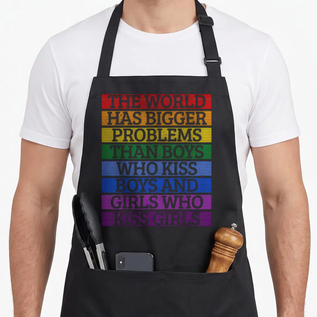 Month gay pride apron - Rainbow horizontal bands with grey text reading The World Has Bigger Problems Than Boys Who — shown on a black cotton canvas apron against a white background