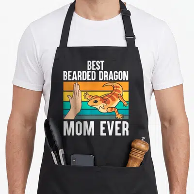 Bearded mother's day aprons - Cartoon bearded dragon high-fiving a hand on orange, yellow, and teal stripes with text — shown on a black cotton canvas apron against a white background