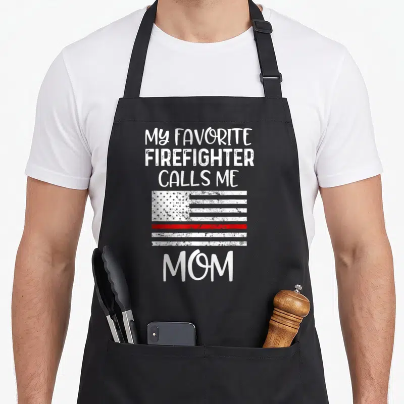 Call firefighter apron - Distressed white flag with thin red line and text MY FAVORITE FIREFIGHTER CALLS ME MOM — shown on a black cotton canvas apron against a white background