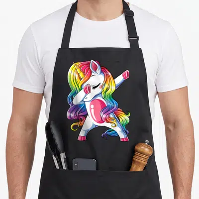 Dabbing rainbow apron - Cartoon unicorn dabbing with white body and rainbow mane in pink, yellow, blue, green, purple — shown on a black cotton canvas apron against a white background