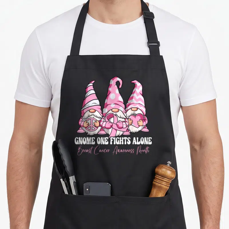 Alone breast cancer awareness aprons - Three pink and white gnomes holding peace sign, ribbon, and heart with text below — shown on a black cotton canvas apron against a white background