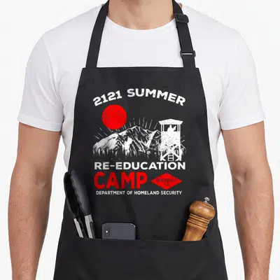 Reeducation camp chef apron - Distressed graphic of red sun, white mountains, watchtower, and text 2121 Summer — shown on a black cotton canvas apron against a white background