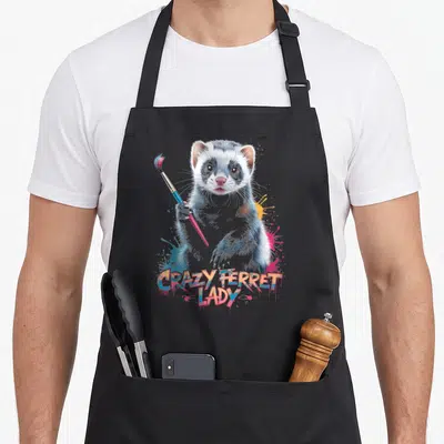 Funny ferret colorful aprons - Realistic ferret holding paintbrush with colorful splatters and graffiti text — shown on a black cotton canvas apron against a white background