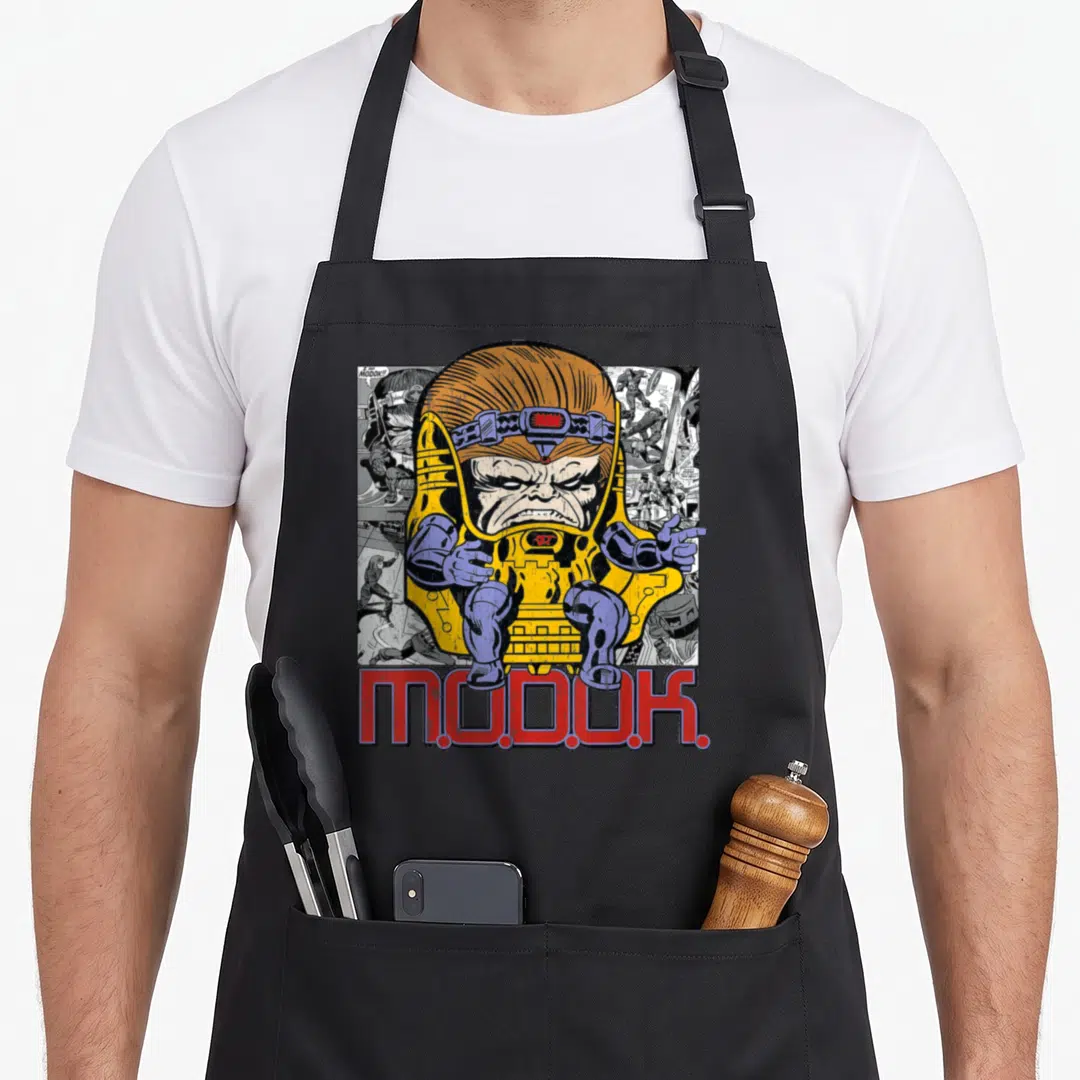 Chillin k apron - MODOK character in yellow chair over comic panels with red M.O.D.O.K. text — shown on a black cotton canvas apron against a white background