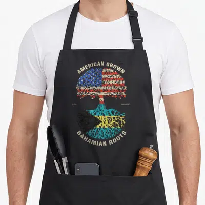 Grown bahamian american flag apron - Tree with American flag canopy and Bahamian flag roots labeled USA and Bahamas — shown on a black cotton canvas apron against a white background