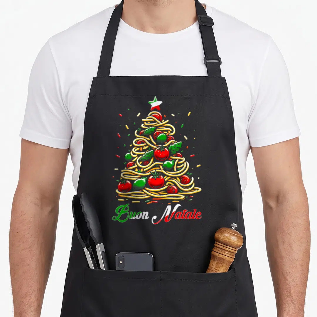 Buon pasta apron - Cartoon pasta Christmas tree with tomatoes and leaves below Buon Natale text in red green and white — shown on a black cotton canvas apron against a white background